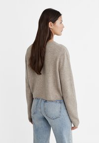 Beige knitted sweater with a cropped design and dropped shoulders, paired with light blue high-waisted denim jeans, viewed from the back.