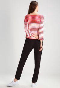 Haut à rayures rouges et blanches à manches longues associé à un pantalon noir et des baskets blanches. Le haut présente un décolleté large et des manches trois-quarts.