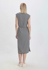 Gestreiftes, ärmelloses Midikleid mit tailliertem Schnitt, aus weichem Stoff gefertigt. Blau und weiße horizontale Streifen, seitlicher Schlitz, kombiniert mit hellen Sneakern.