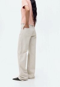 Pantalon à jambes larges beige clair avec taille haute et poches arrière, associé à un haut rose texturé. Tissu lisse, design minimaliste.