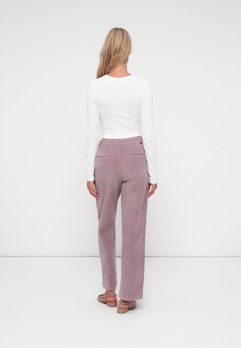 Pantalones de pana de color púrpura claro con piernas anchas, bolsillos traseros y una blusa blanca de manga larga cortada. Vista trasera, con un fondo sencillo.