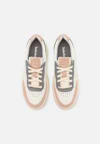 Sneaker blanche avec des accents gris et rose. Fabriquée en cuir et en daim, elle possède des lacets ronds, des perforations sur la pointe, et un logo sur la languette.