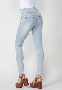 Jeans ajustados de color azul claro con una cintura alta, que presentan dos bolsillos traseros y detalles de costura sutiles. Combinados con sandalias de plataforma marrones.