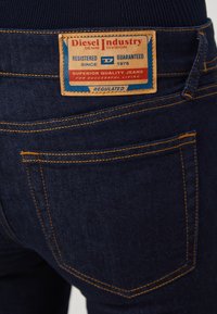 Mörka denimjeans har en synlig varumärkesetikett och kontrasterande gula s ömmar. Fickorna och texturen framhävs i närbild.