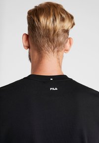 Černé bavlněné tričko s kulatým výstřihem a malým bílým logem FILA potisknutým na zadní straně, se softovou texturou a volným střihem.