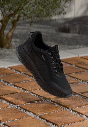 Zwarte sport sneaker met een getextureerde mesh bovenkant, geperforeerde details en rubberen zool. Veters zijn door versterkte oogjes geweven.
