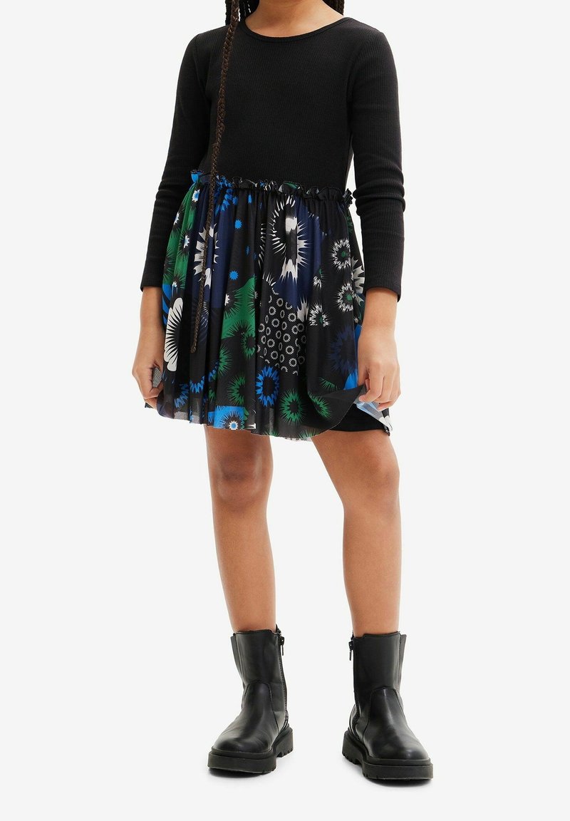 Haut à manches longues noir avec jupe plissée arborant des motifs floraux bleus, verts et blancs ; accompagné de bottines noires.