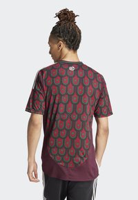 Camiseta de manga corta color marrón con un patrón verde y negro en la parte posterior, con un escote redondo y franjas laterales contrastantes.