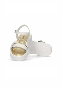 Witte platform sandalen met een gouden metalen band en verstelbare enkelgesp. Getextureerde witte zool zorgt voor stabiliteit en grip.