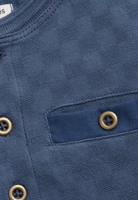 Blauer, strukturierten Stoffabschnitt eines Hemdes mit Messingknöpfen und einer dunkelblauen Stofftaschenklappe mit einem Messingknopf.