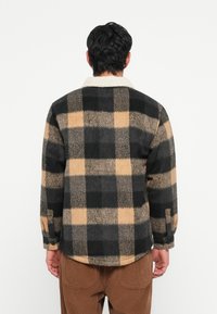 Black and beige plaid flannel jacket with a soft, textured finish and a cream collar. Relaxed fit and rounded hem.