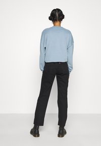 Felpa oversize blu chiaro abbinata a jeans neri a gamba dritta. Presenta un'etichetta con logo sulla schiena e stivali neri alla caviglia.