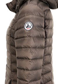 Takkihousu tummanruskeana, jossa on tikattu rakenne, huppu ja olkapäällä ympyrälogo, jossa on koira-design.