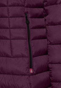 Bordeaux pufferjack met een geborduurd ontwerp, zwarte ritsdetails en een klein merklabel in roze nabij de rits. Textuurstof.