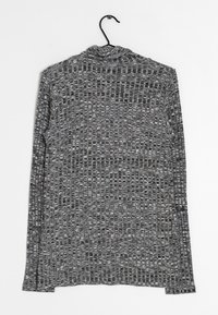 Šedá strukturovaná košile s dlouhým rukávem a vysokým límcem, s vzorem malých čtverců a obdélníků. Zavěšena na černém háčku.