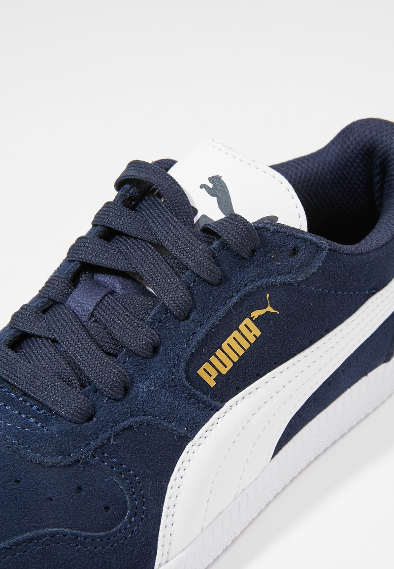 Baskets en daim bleu marine avec des accents blancs, arborant un logo doré "PUMA", un design à lacets et une semelle en caoutchouc texturée.