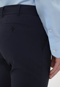 Sötétkék nadrág sima anyagból, gombos záródással, egyetlen hátsó zsebbel és áramvonalas dizájnnal.