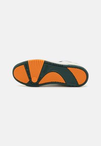 Shoe sole featuring a textured orange rubber base with hexagonal patterns, dark green accents, and a segmented tread design for grip.