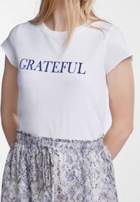 Camiseta de algodón blanca con la palabra "GRATEFUL" impresa en azul marino, combinada con una falda estampada que presenta tonos de azul y gris.
