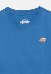 Μπλε μπλουζάκι με στρογγυλή λαιμόκοψη που διαθέτει ένα μικρό λογότυπο Dickies στο αριστερό στήθος και μια μεγαλύτερη ετικέτα λογότυπου στο εσωτερικό της λαιμόκοψης.