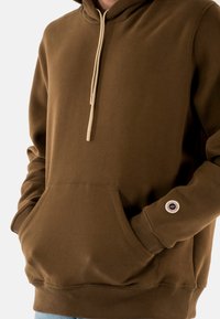 Felpa con cappuccio marrone realizzata in tessuto morbido, con tasca frontale, polsini a coste e cappuccio con cordino e accenti beige.