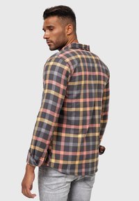 Camisa de cuadros en gris, naranja y amarillo, con mangas largas, puños abotonados y un cuello clásico. Tejido suave con un diseño ajustado.