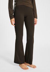 Brązowe spodnie o szerokich nogawkach, wykonane z elastycznego materiału. Gładka tekstura, dopasowany pas, szwy biegnące wzdłuż nóg oraz długość do kostek.