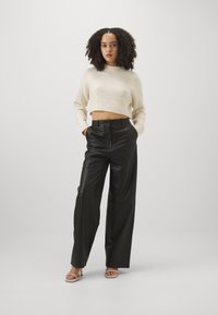 Cream cropped sweater and black high-waisted leather trousers, featuring a smooth texture and wide-leg design, paired with light heels.