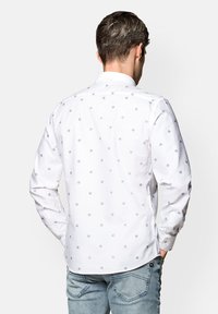 Biała koszula z guzikami, ozdobiona małymi niebieskimi wzorami kwiatowymi, z długimi rękawami i kołnierzykiem. Materiał wydaje się gładki z lekkim połyskiem.