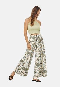 Top corto de canalé verde claro combinado con pantalones de pierna ancha con estampado floral en crema, que cuentan con una cintura con lazo y sutiles franjas laterales.