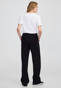 Czarne spodnie typu wide-leg o gładkiej fakturze, z przednimi kieszeniami i elastycznym paskiem w talii, zestawione z gładką, białą bluzką z krótkim rękawem.