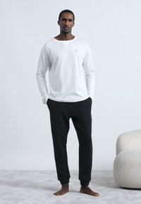 Λευκό μακρυμάνικο πουκάμισο και μαύρο φόρμα παντελόνι, κατασκευασμένα από απαλό ύφασμα. Το πουκάμισο έχει στρογγυλή λαιμόκοψη· το παντελόνι διαθέτει ελαστική μέση.