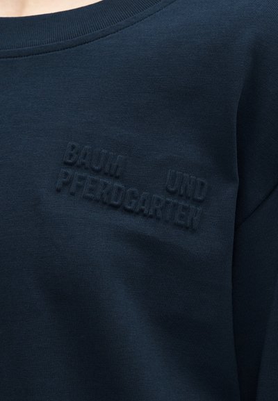 Κοντινή λήψη σκούρου μπλε φούτερ με ανάγλυφο κείμενο «BAUHAUS UND PFERDOCARTEN» στην περιοχή του στήθους.