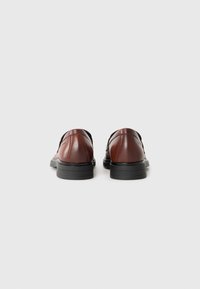 Brown leather shoes with a smooth texture, featuring a low black rubber sole, back view showing structured heel and rounded toe design.