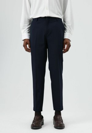 Marineblauwe, op maat gemaakte broek van lichtgewicht stof, met een slanke pasvorm en een subtiele plooi aan de voorkant, gecombineerd met donkerbruine loafers.