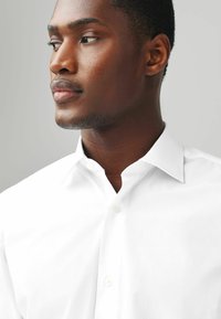 Chemise blanche à col classique, texture lisse et satinée, avec une fermeture boutonnée à l'avant et un tissu bien repassé.