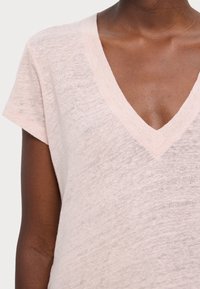 Světle růžové tričko s V-výstřihem a krátkými rukávy, vyrobené z měkké, texturované tkaniny, s jemným melírovaným vzorem a pečlivým prošitím.