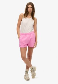 Roze katoenen shorts met elastische tailleband en zijzakken, gecombineerd met een lichtgrijze mouwloze top en beige sneakers met groene accenten.
