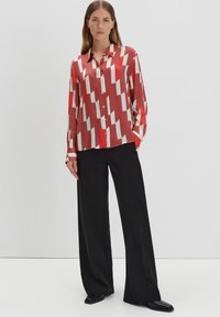 Rode en witte geometrische geblokte zijden blouse met een knoopsluiting aan de voorkant, lange mouwen en een kraag, gecombineerd met zwarte wijde broekspijpen.