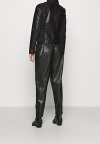 Czarna skórzana kurtka w krótkim kroju z dopasowanym fasonem, w połączeniu z luźnymi czarnymi skórzanymi spodniami i masywnymi botkami na obcasie. Gładka tekstura na całej powierzchni.