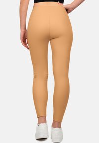 Leggings beige con una vita alta, design aderente e texture liscia. L'abbinamento con sneakers bianche completa il look.