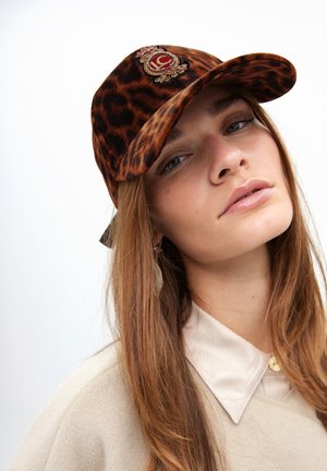 Gorra de estampado de leopardo hecha de terciopelo, con un emblema bordado en tonos dorados y una visera curva. El interior tiene un color contrastante.