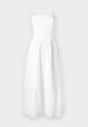 Vestido maxi de linho branco com alças spaghetti ajustáveis, parte superior franzida e saia em camadas. Textura leve para conforto e respirabilidade.