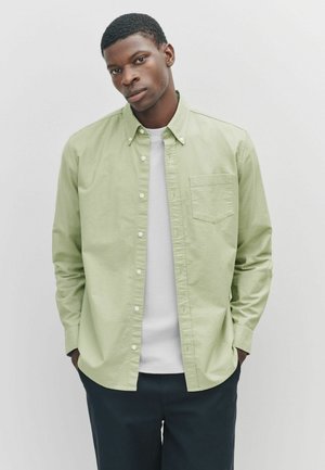 Hellgrünes Hemd aus Baumwolle mit Knopfleiste, verfügt über eine Brusttasche, einen Button-Down-Kragen und lange Ärmel, kombiniert mit einem weißen T-Shirt.