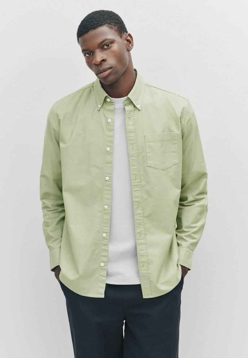 Lichtgroene knoopshirt van katoen, met een borstzak, een button-down kraag en lange mouwen, gedragen met een witte T-shirt.