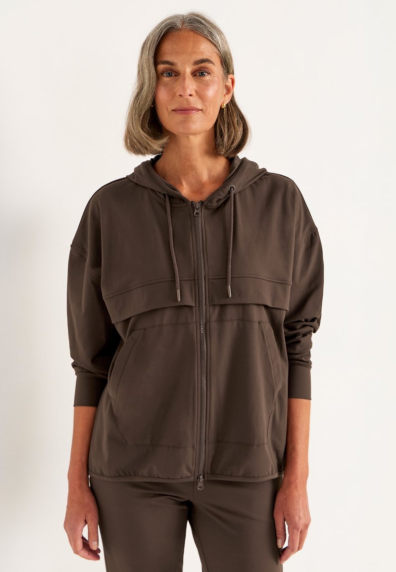 Brauner Reißverschluss-Hoodie aus weichem Material, mit einem doppellagigen Design auf der Brust, vorderen Taschen und gerippten Bündchen.