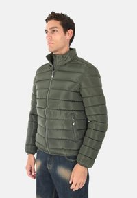 Giubbotto imbottito di colore verde scuro, con zip frontale, colletto alto e cuciture orizzontali. Tessuto testurizzato e leggero con tasche laterali.