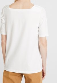 Top blanco de manga corta con escote cuadrado, hecho de una tela suave. La parte posterior presenta un diseño limpio sin adornos.
