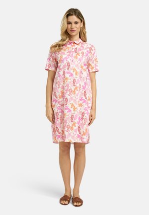 Woman wearing a short-sleeve, knee-length dress with pink, orange, and red zebra patterns paired with brown sandals.