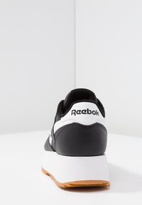 Czarno-biały sneaker z cholewką zamszową i syntetyczną, grubą białą podeszwą środkową, gumową podeszwą oraz logo "Reebok" na pięcie.